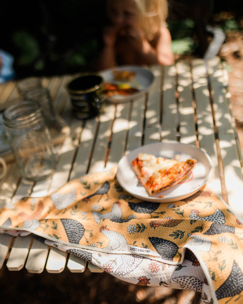 Farmhouse Chicken Kitchen & Tea Towel resting on a table during a family meal outdoors.