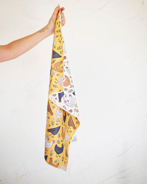 Farmhouse Chicken Kitchen & Tea Towel being held with colorful chicken design on a yellow background.