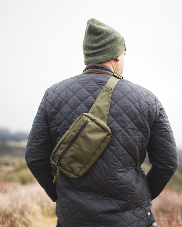 Man wearing Everyday Fanny Pack (Fern) as a crossbody sling, showcasing its versatility in outdoor setting.