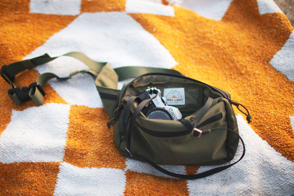 Everyday Fanny Pack (Fern) on a picnic blanket, showcasing its spacious and versatile design with multiple pockets and zippers.