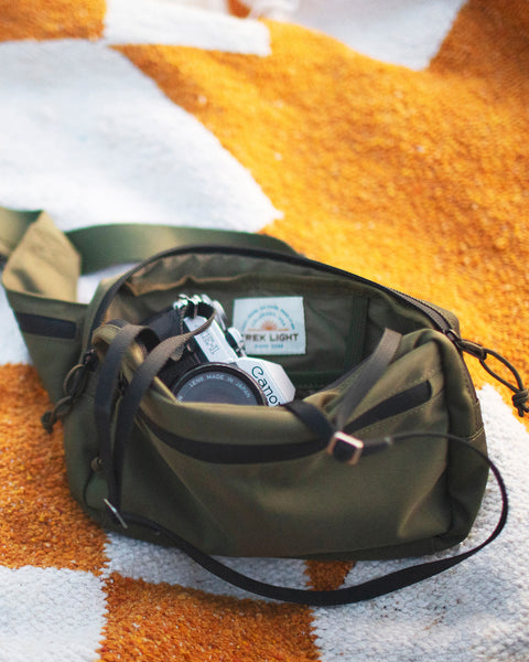 Everyday Fanny Pack (Fern) on a picnic blanket, showcasing its spacious and versatile design with multiple pockets and zippers.