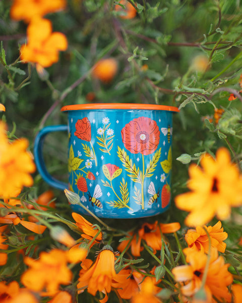Trek Light 16oz Garden Buzz Enamel Mug amidst vibrant orange flowers, perfect for outdoor adventures.