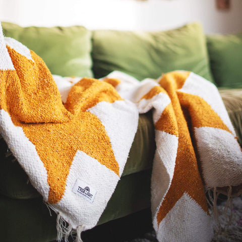 Cozy handwoven Goldie blanket with geometric design, made from recycled clothing materials, draped over a green sofa. By Trek Light.