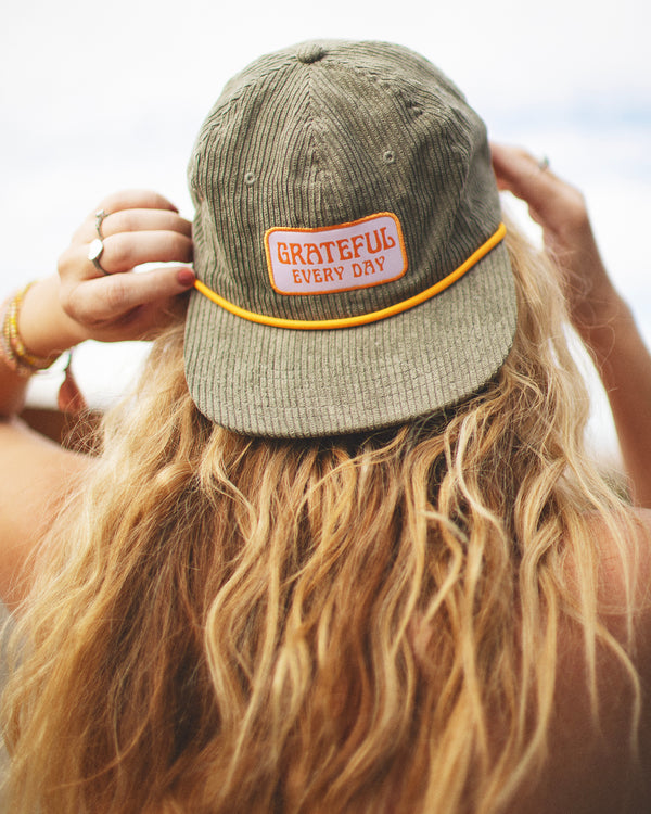 Person wearing Trek Light Grateful Every Day hat with flat brim and corduroy style, perfect for expressing gratitude and style.