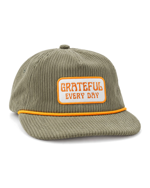 Grateful Every Day Hat in olive green corduroy with a golden yellow rope trim and a white and orange patch, on white.