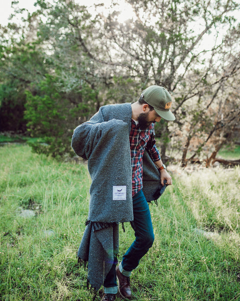 Man outdoors holding the Greyson Blanket in a green field, showcasing its sleek and modern design.