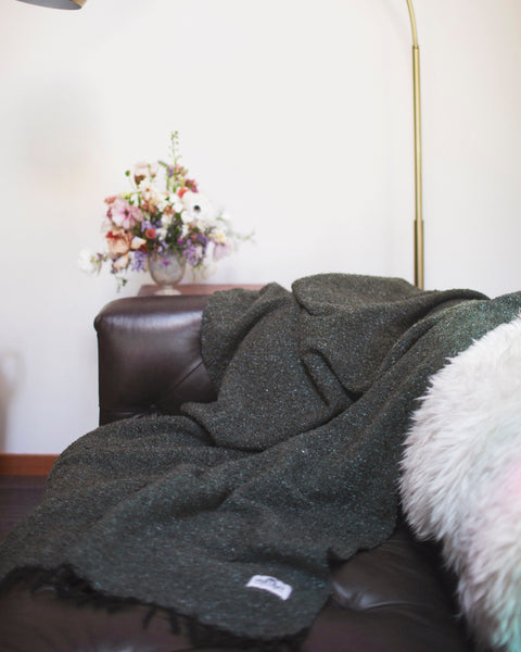 Greyson Blanket draped on a leather couch next to a floral arrangement, showcasing its sleek and modern design.