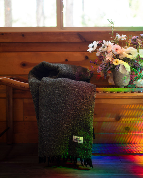 Greyson Blanket draped over a wooden bench near a flower arrangement in a cozy setting.