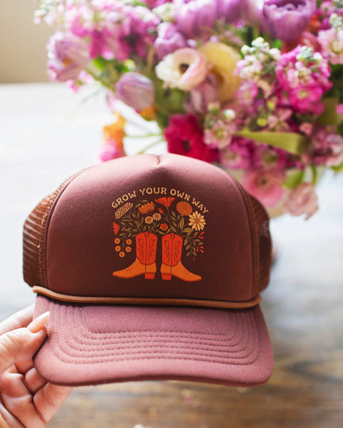 Hand holding the Grow Your Own Way Hat featuring floral design and boots, perfect for stylish comfort.