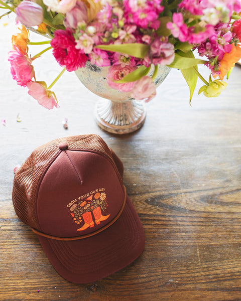 Grow Your Own Way Hat on a wooden table beside a floral arrangement, capturing vibrant colors and unique design.