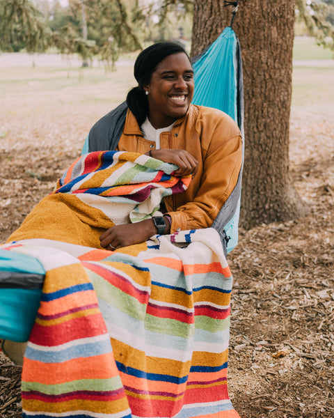 Person enjoying the outdoors wrapped in a Halley's Comet Blanket with colorful stripes.