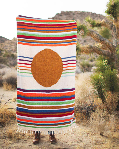Person holding the Halley's Comet Blanket, colorful striped design with a circle pattern, ideal for outdoor use.