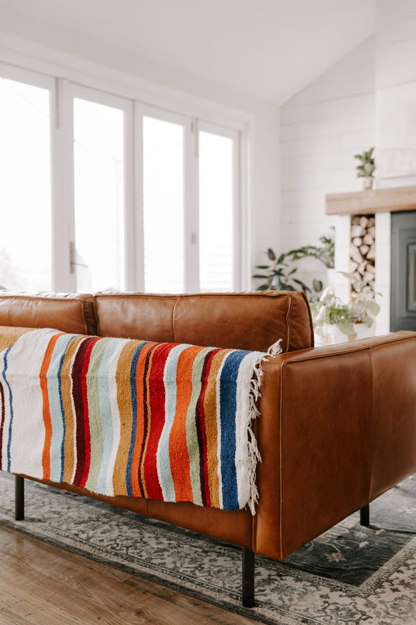 Vibrant Halley's Comet Blanket by Trek Light draped over a cozy brown leather sofa in a well-lit, stylish living room.