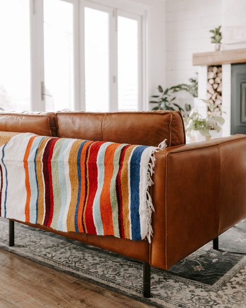 Vibrant Halley's Comet Blanket by Trek Light draped over a cozy brown leather sofa in a well-lit, stylish living room.