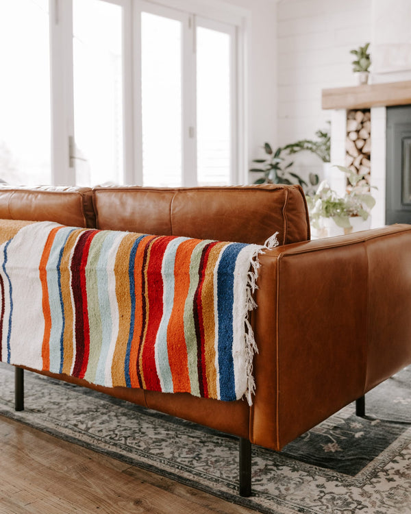 Vibrant Halley's Comet Blanket by Trek Light draped over a cozy brown leather sofa in a well-lit, stylish living room.