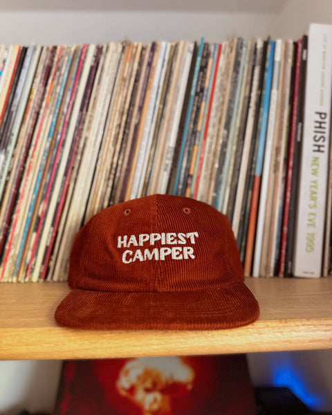 Happiest Camper Hat displayed on a shelf with vinyl records in the background, showcasing its stylish corduroy design.