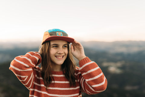 Girl wearing a Happiest Camper Kids Hat enjoying the outdoors with mountains in the background.