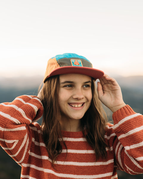 Girl wearing a Happiest Camper Kids Hat enjoying the outdoors with mountains in the background.