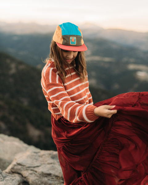 Girl wearing Happiest Camper Kids Hat outdoors with mountains in the background, enjoying nature.
