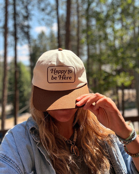 Person wearing a Happy To Be Here Hat outdoors, showcasing a stylish and comfortable vibe.