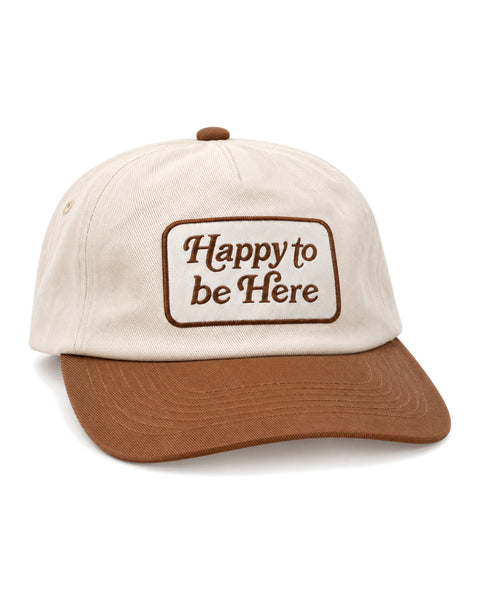 Happy To Be Here Hat in cream with a brown brim and a brown embroidered patch reading "Happy to be Here," on white.
