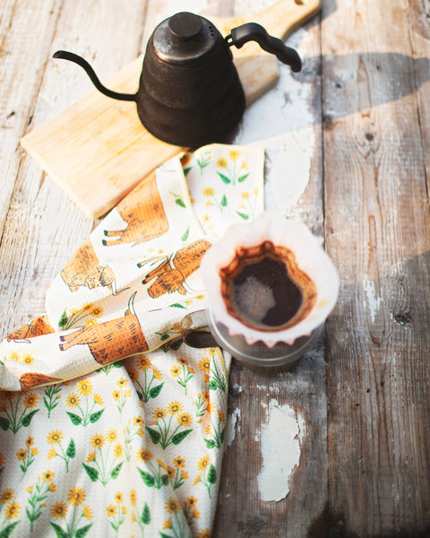 Highland Cows Kitchen & Tea Towel displayed with coffee kettle and mug on a rustic wooden table.