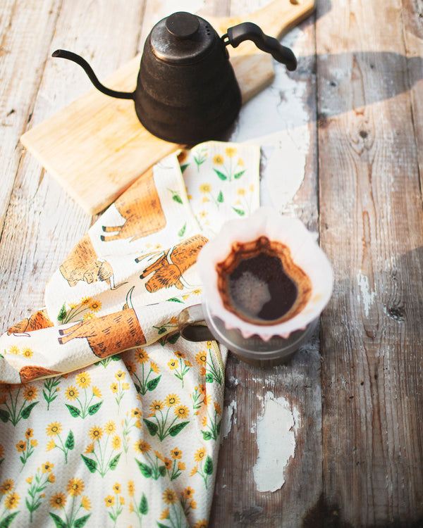 Highland Cows Kitchen & Tea Towel displayed with coffee kettle and mug on a rustic wooden table.