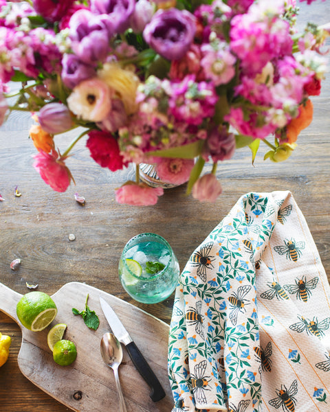 Honey Bee Kitchen & Tea Towel on a wooden table with limes, knife, and a glass of drink.