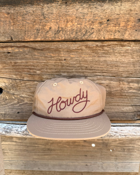 Howdy Hat, Twinsie Set, a tan nylon cap with brown script Howdy embroidery and rope trim, on a weathered wood plank wall.