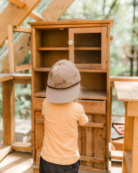 Child exploring wooden cabinet wearing Howdy Kids Hat, showcasing fun and adventure in outdoor play.