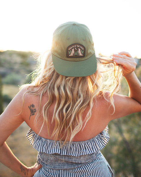 Woman wearing Howlin' At The Moon Hat against a sunset backdrop, showcasing style and comfort.