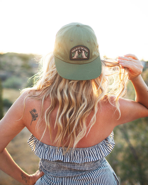 Woman wearing Howlin' At The Moon Hat against a sunset backdrop, showcasing style and comfort.