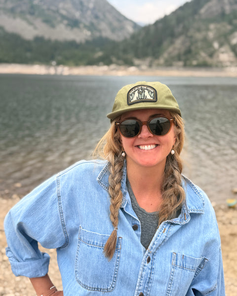 Woman wearing Howlin' At The Moon Hat by a lake, ready for outdoor adventures.