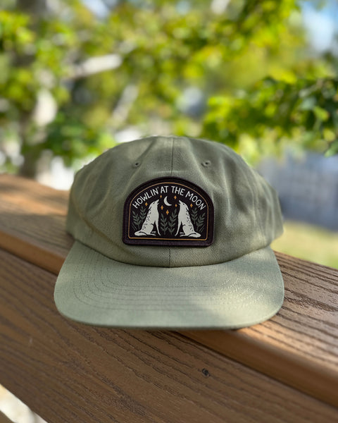 Trek Light Howlin' At The Moon Hat on wooden ledge with forest background, perfect for adventurous spirits and wild howlers.