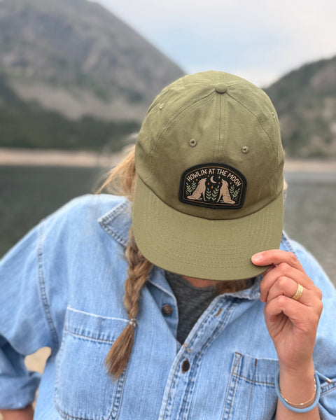 Person wearing a Howlin' At The Moon Hat near a lake with mountains in the background.