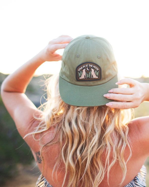 Woman wearing a Howlin' At The Moon Hat against a sunset backdrop, showcasing style and comfort.
