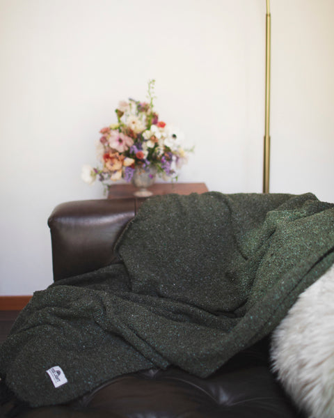 Humboldt Blanket draped over a couch with a lampshade and a bouquet of flowers in the background.