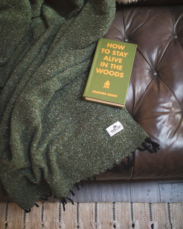 Cozy Humboldt Blanket draped over a leather couch with 'How to Stay Alive in the Woods' book, handwoven and eco-friendly design.