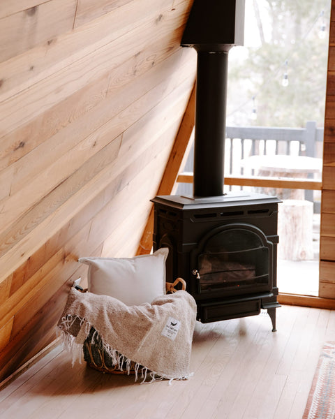 Cozy Huntington Blanket by Trek Light near a wood stove in a rustic cabin setting, perfect for beach or campfire nights.