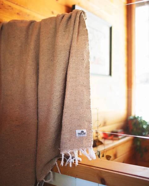 Huntington Blanket hanging on a wooden rail, showcasing its cozy beach vibes in a warm interior setting.