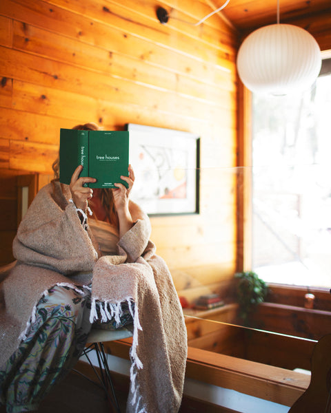 Cozy scene featuring a person wrapped in a blanket reading a book in a wooden cabin, ideal for relaxing moments.