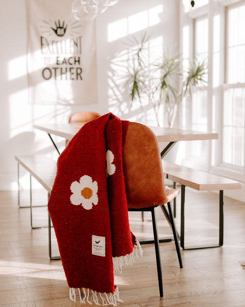 Cozy red Lazy Daisy Blanket on a chair, featuring a charming daisy print. Perfect for slowing down and savoring life's lazy moments. Trek Light.