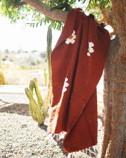 Lazy Daisy Blanket hanging from a tree, showcasing its vibrant design in a natural outdoor setting.