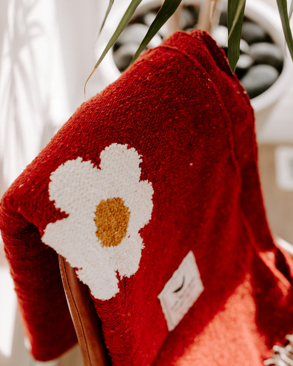 Cozy red blanket with a white daisy design draped over a chair, embodying Trek Light's Lazy Daisy vibe.
