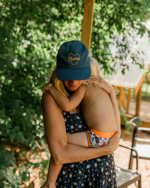 Mama Hat worn by a mother embracing her child in a lush, green setting.