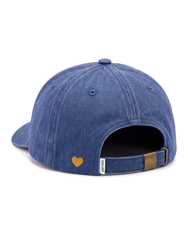 Mama Hat in blue denim, seen from the back, with a small gold embroidered heart and a brass strap buckle, on white.