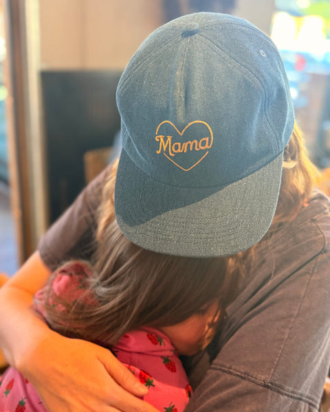 Mama Hat with heart embroidery worn by a person embracing a child, showcasing comfort and style.
