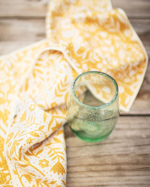 Meadow Kitchen & Tea Towel draped with a green glass on rustic wooden surface.
