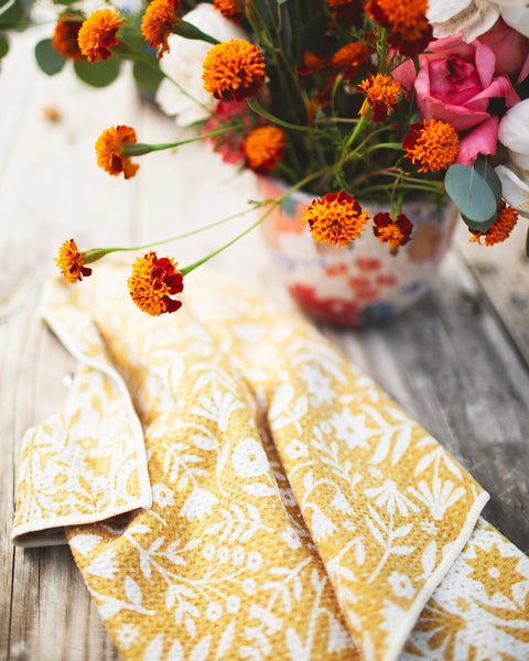 Meadow Kitchen & Tea Towel with vibrant floral design and hanging loop beside a flower pot.