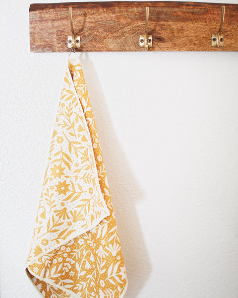 Meadow Kitchen & Tea Towel hanging on a wooden hook, showcasing floral design and vibrant colors.